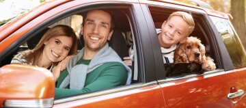 Glückliche Familie mit Kind und Hund in einem orangefarbenen Auto auf einem sonnigen Ausflug