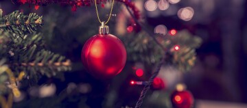 Nahaufnahme eines Weihnachtsbaums mit rotem Christbaumschmuck und warmen Lichtern im Hintergrund