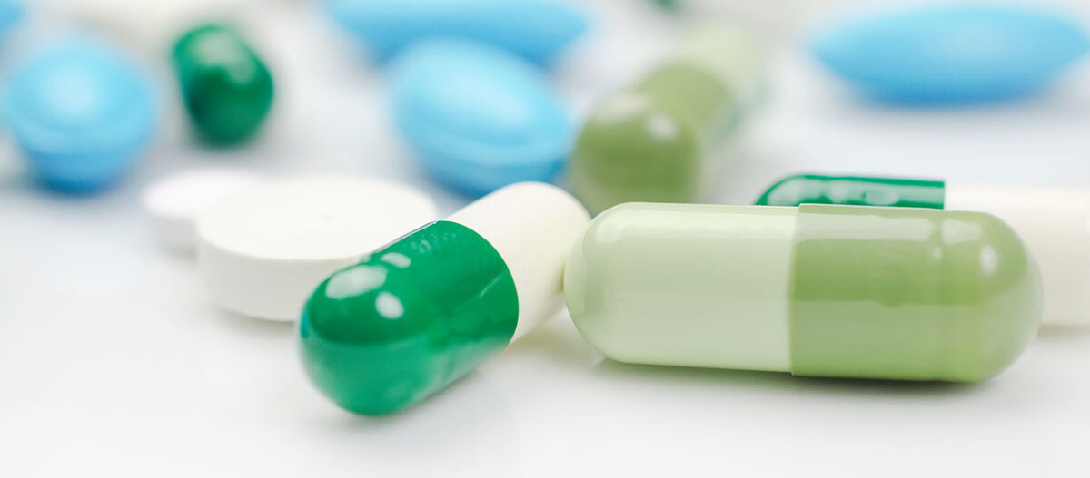 Hundeapotheke: Tabletten Nahaufnahme von grünen und weißen Kapseln sowie blauen und weißen Tabletten auf weißem Hintergrund, medizinische Medikamente