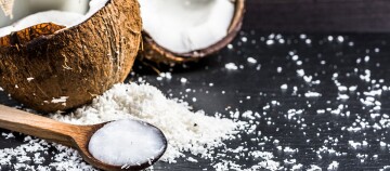 Frische Kokosnusshälften mit geraspeltem Kokosnussfleisch auf dunklem Untergrund und Holzlöffel