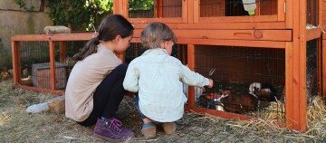 Zwei Kinder sitzen vor einem Stall mit Meerschweinchen.
