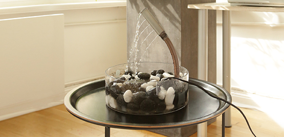 Moderner Indoor-Wasserbrunnen mit schwarzen und weißen Steinen auf rundem schwarzen Tisch in hellem Raum