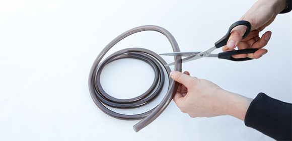 Person schneidet braunen Gummischlauch mit Schere auf weißem Hintergrund