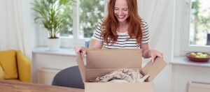 Glückliche junge Frau öffnet ein Paket mit Verpackungsmaterial in einem hellen Wohnzimmer