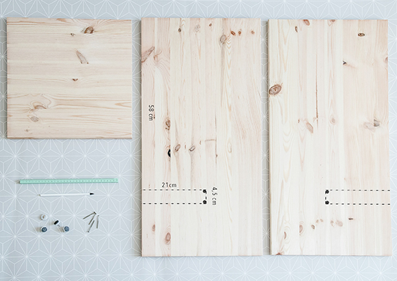 Anleitung DIY Katzenhaus Drei helle Holzplatten mit Maßen und Schrauben auf gemustertem Untergrund für ein DIY-Projekt