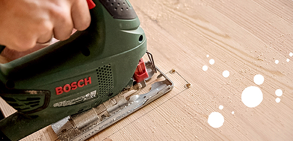 Anleitung DIY Katzenhaus Person schneidet Holz mit Bosch Elektrostichsäge präzise entlang einer Markierung