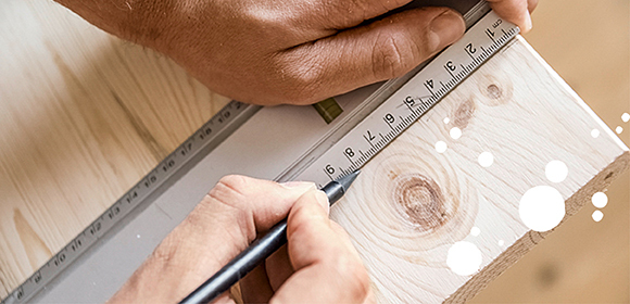 Anleitung DIY Katzenhaus Hand misst und markiert Holz mit Lineal und Bleistift für präzises Schreinerarbeiten