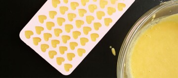 Silikonform mit kleinen herzförmigen Teigstücken und Schüssel mit gelber Mischung auf schwarzem Hintergrund