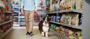 Mann mit Hund an der Leine beim Einkaufen in einem Zoofachgeschäft mit Regalen voller Tierfutter