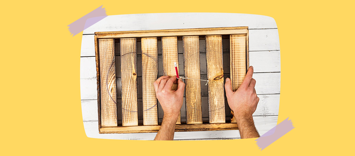 Person zeichnet mit Schnur und Bleistift einen perfekten Kreis auf eine Holzpalette vor weißem Holzhintergrund