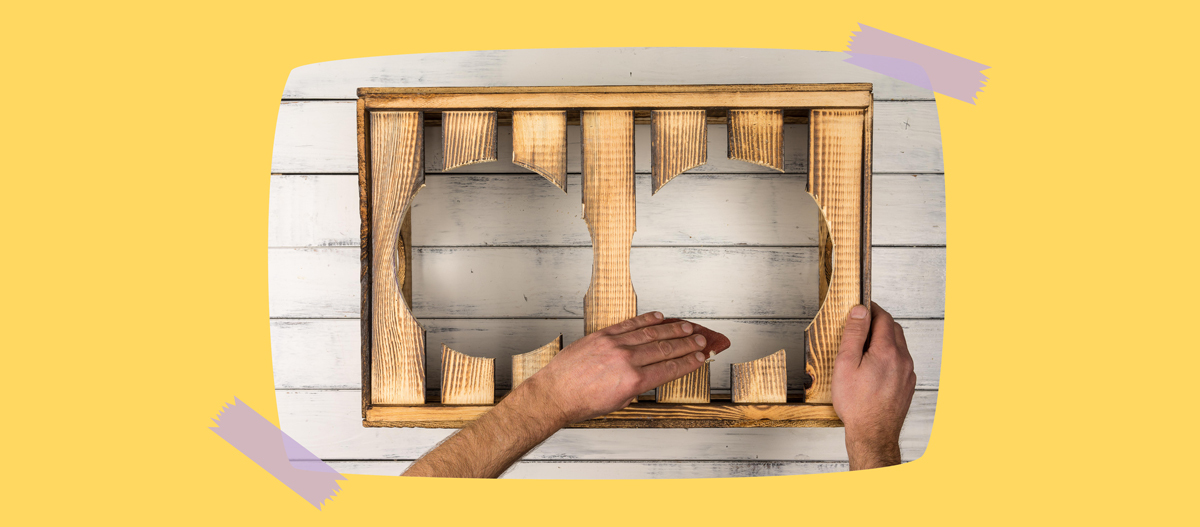 Mann schleift hölzernen Kasten mit Ausschnitten auf weißem Holztisch, kreative gelbe Hintergrundgestaltung