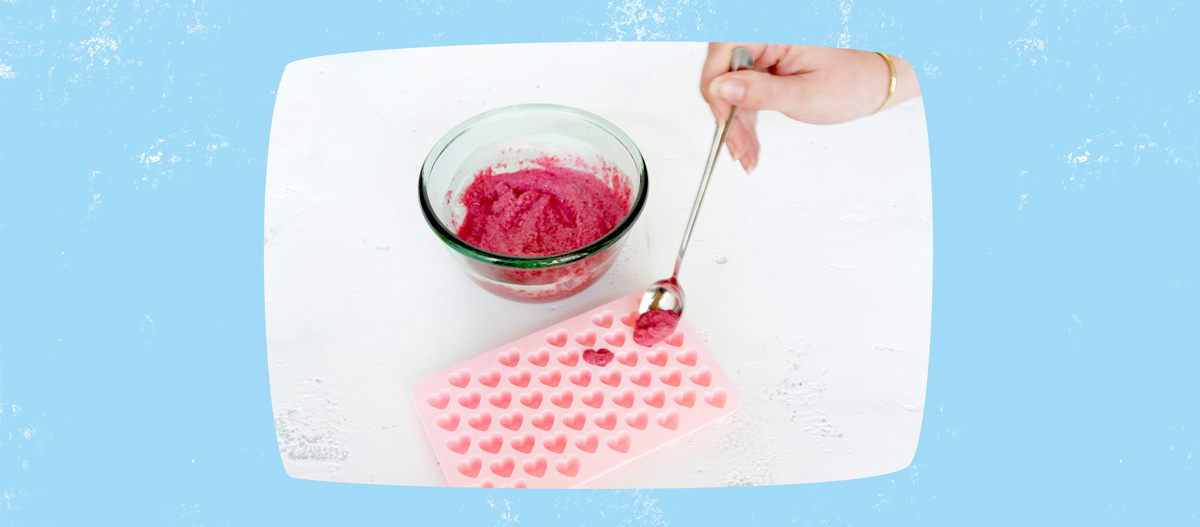 Hand füllt rosa Silikonform in Herzform mit pinker Mischung aus Glasschüssel für selbstgemachte Bonbons oder Badebomben