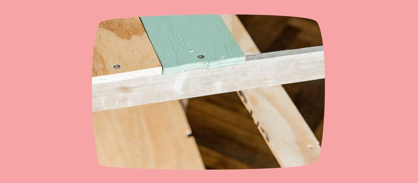 Nahaufnahme eines Holzrahmens mit grün gestrichenem Brett und Schrauben, unvollendetes Möbelstück oder Bauprojekt