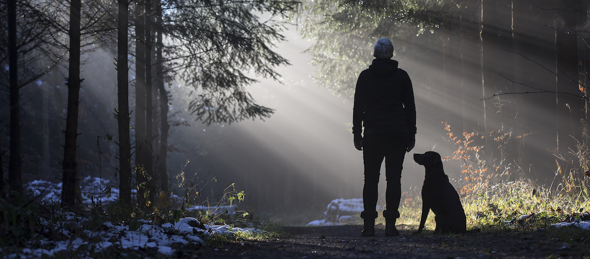 Frau steht mit Hund im Winterwald
